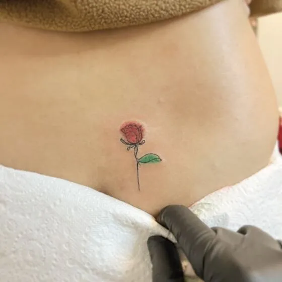 Fine line single-line red rose tattoo on the hip