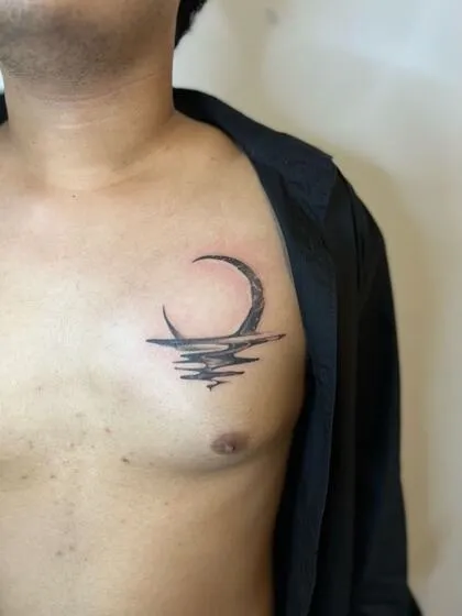 Black and grey crescent moon reflected on ocean ripples, chest tattoo