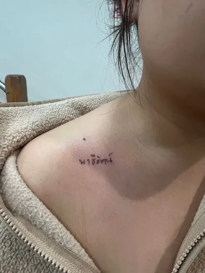 Fine line Thai script name tattoo on the collarbone