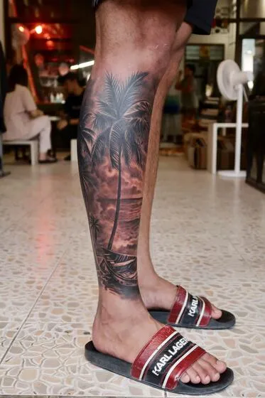 Realism leg tattoo of a tropical beach with a Thai longtail boat