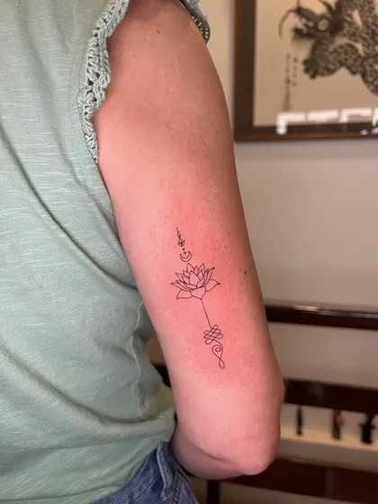 Fine line unalome rising from a lotus on the back of the upper arm