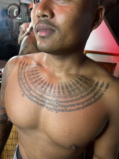 Rows of Khom yantra script fanning across the chest below the collarbones