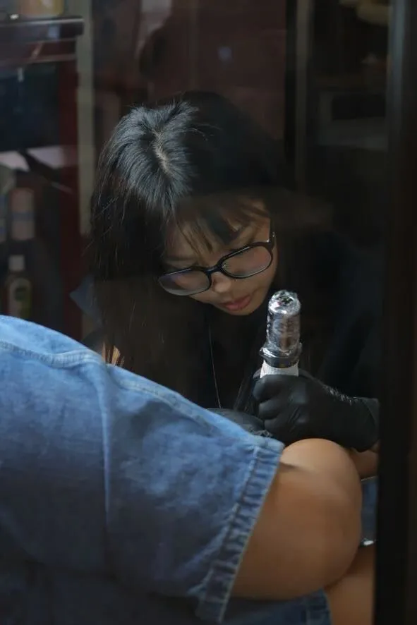 A Beach Street Arts artist tattooing in gloves and glasses